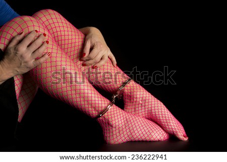 A woman with her legs in pink fishnet stockings and cuffs on her ankles and her hands on her legs.