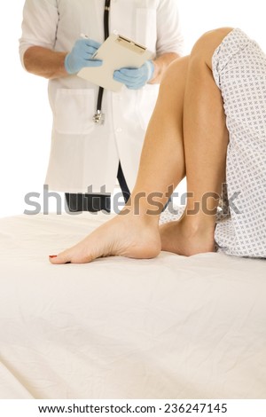 A doctor writing on a clipboard by the legs of a woman patient.