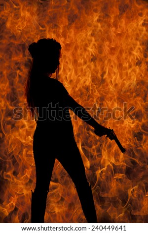 a silhouette of a woman with a fire back ground pointing her gun to the ground.