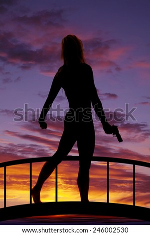 a silhouette of a woman walking on a bridge holding on to a pistol.