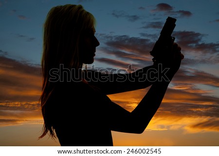 a silhouette of a woman holding onto a pistol looking forward.