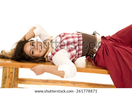 a woman laying back on a bench in her western wear with a smile.
