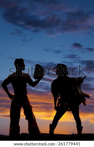 a silhouette of a cowgirl holding her saddle while her cowboy takes off his hat.