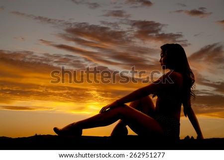 A silhouette of a woman sitting up in her bikini looking to the side.