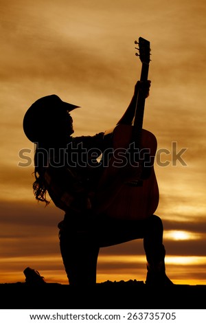 a silhouette of a woman kneeling with her guitar.