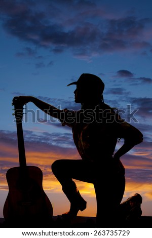 a silhouette of a cowgirl kneeling down next to her guitar.