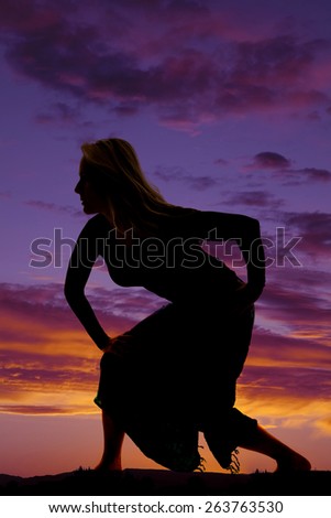 A silhouette of a woman crouching down in her sarong as she walks.