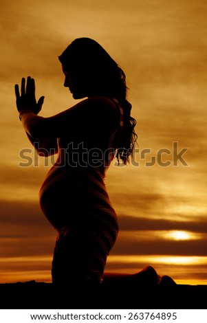 a silhouette of a girl on her knees praying with her belly showing.