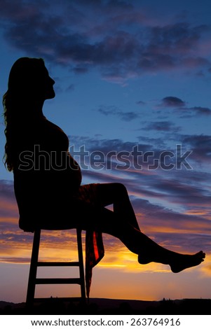 A silhouette of a pregnant woman sitting on a stool relaxing