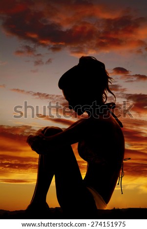 A silhouette of a woman in her bikini curled up in a ball.
