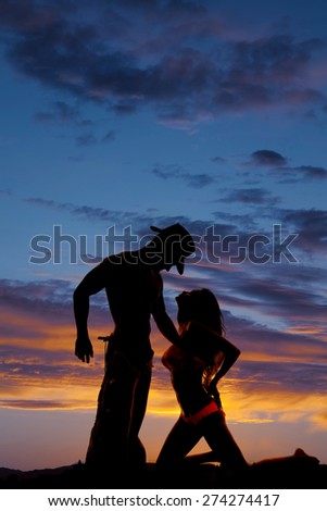 A silhouette of a woman on her knees looking into her cowboys face.