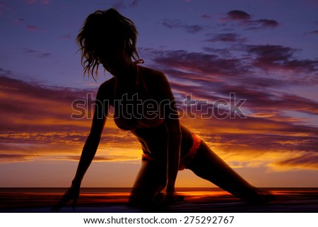 A silhouette of a woman kneeling in the outdoors in her bikini.