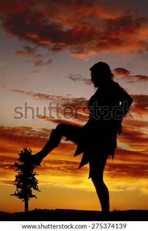 A silhouette of a cave woman with her foot on a tree.