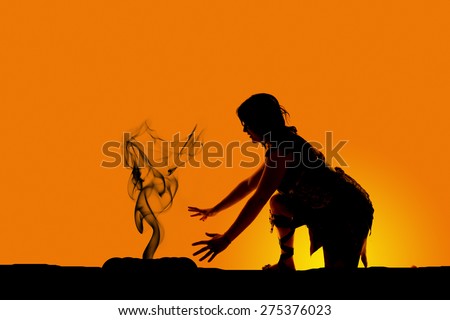 A silhouette of a cave woman kneeling down by a fire.