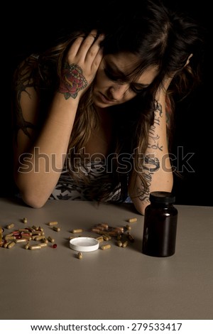 A woman with a depressed expression on her face, looking down at the drugs on the table.