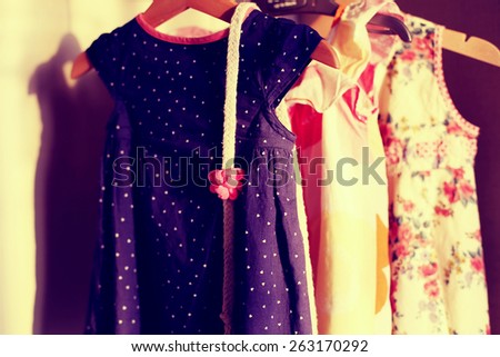 Closet with colorful baby dresses on hangers. Cotton baby belt on a dress in wardrobe with retro vintage view