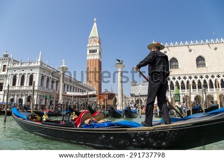 Venice, Italy - April 23, 2015: Unidentified gondolier wearing traditional dress in the gondola and sail on a Venetian canal near Campanile and Doge\'s palace on Saint Marco square in Venice, Italy