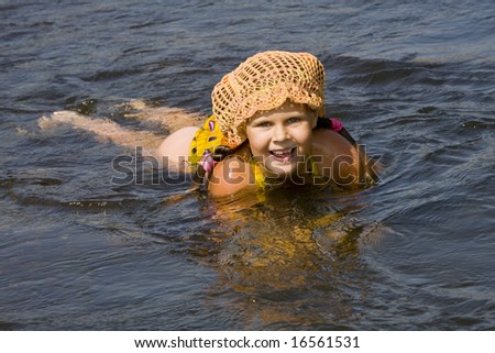 Little girl in orange hat swimming in a river in the summer