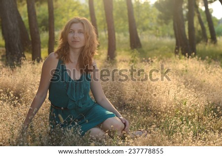 Portrait of a red-haired beautiful woman in green dress sitting in the bunny tail grass