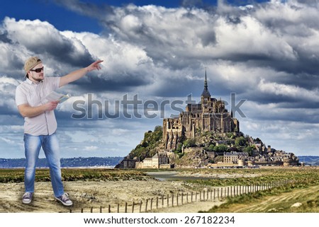 Man with guide book in a hand with Mont Saint-Michel, Lower Normandy, France in background