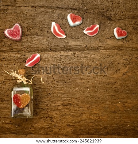 Valentines day card, bottle and gummy hearts on old wooden background with space for writing message or put photos