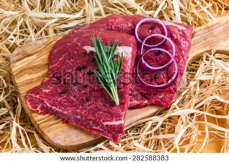 British Beef Flat Iron steak on cutting board and straw, rosemary and onion.