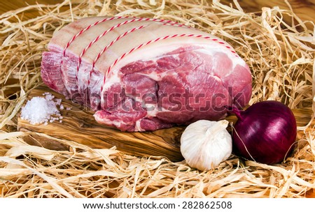 Farm British Boneless Pork Shoulder on cutting board and straw, onion, garlic and Sea salt.