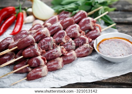 Ready to cook Duck Heart stringed on skewers BBQ with hot sauce and chili pepper. decorated with greens and vegetables.  background