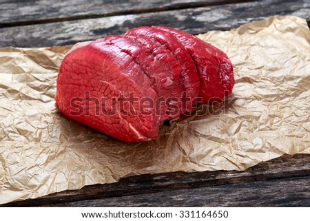 a pieces of fresh meat, beef slab on crumpled paper on old wooden table. ready to cook