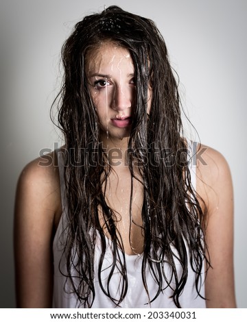 Portrait of a beautiful young teenage girl with water streaming down her face and hair. Wet skin. Isolated against a light grey background.