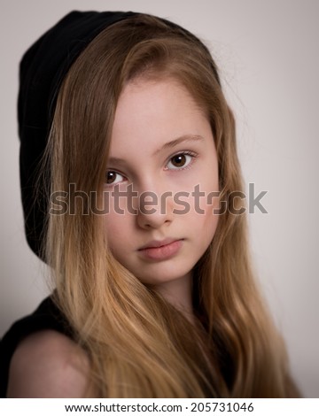 Portrait of a beautiful young girl with long blond hair, brown eyes, wearing a hoodie jumper isolated against a grey background.