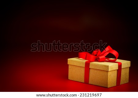 A closed golden surprise present box with a red ribbon isolated against a black and red background