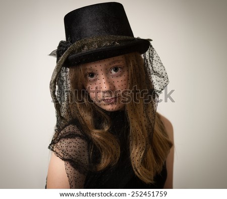 Portrait of a beautiful ginger teenage girl with long hair wearing a vintage victorian horse riding hat with veil isolated against a grey background.