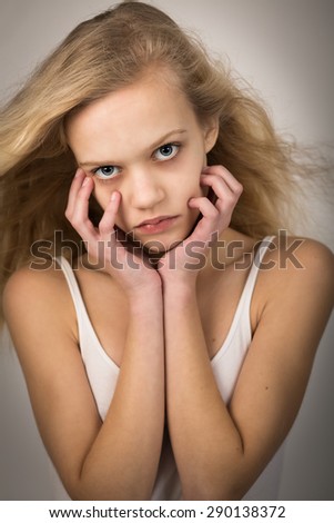 Studio shot of a beautiful teenage girl with long hair blowing in the wind with her hands on her face looking into the camera.