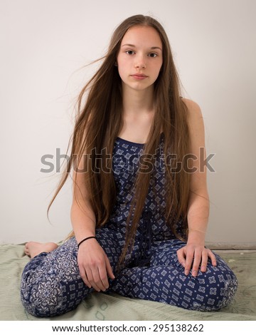 Portrait of a beautiful teenage brunette girl with extremely long hair sitting on the floor in blue pajamas looking in the camera.