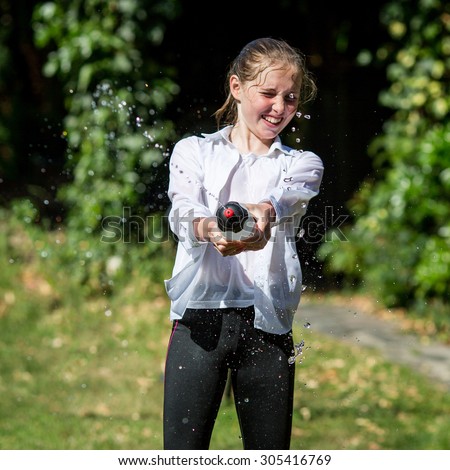 Wet teenage girl in white shirt and black legging squeezes water from plastic bottle.