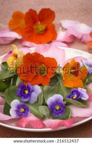 salad of edible flowers in ceramic dish. colorful summer dish. with nasturtiums, pansies, roses and mache.