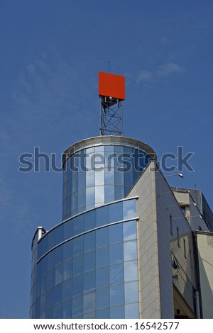 Red square billboard on top of the modern glass building.