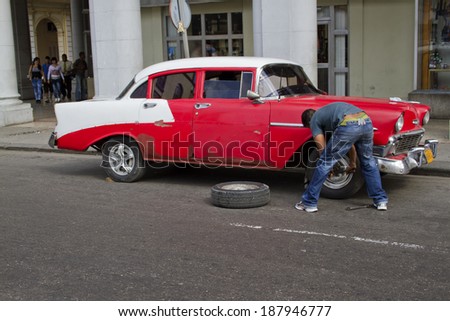 Havana, Cuba - December 25, 2010; Red classic car in Havana, Cuba, with with its tire being changed.  Past international embargoes have meant Cuba has maintained many pre-revolutions vehicles.