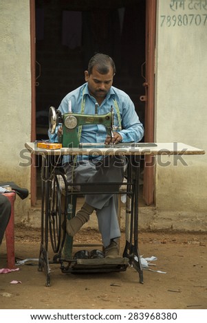 Orccha, India - January 3, 2015; Man sewing with an old sewing machine outside his shop. In small villages in India people use old fashioned peddle sewing machines.