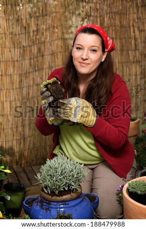 Woman with a red headscarf gardening gand repoting in front of a bamboo fence