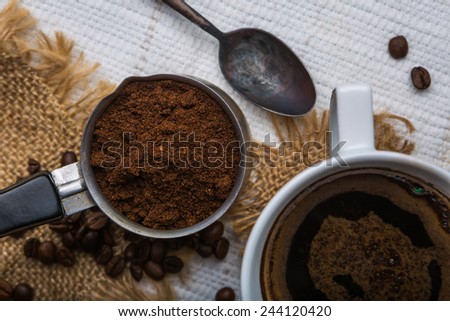 Ground coffee with coffee beans and cup of coffee on wooden background