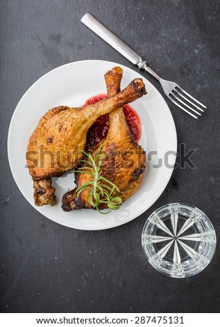 Roast duck legs with cranberries and fresh rosemary on white plate