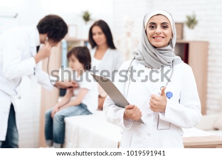 An Arab doctor in hijab poses with a history of the disease in his hands. In the back, the man examines the sick boy. He came to the hospital with his mother, because he fell ill.