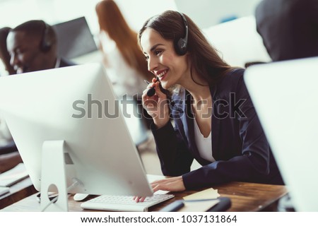 Caucasian girl looks at work in the call center. She answers customer calls. She\'s in a good mood.