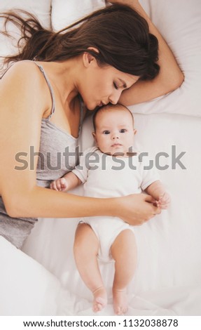 Top view. Happy Young Mother with Baby in Bed. Little Newborn Child in White Bed. Parenthood Concept. Love and Happiness. Taking Care of New Life. Family, Love, Happiness Concepts.