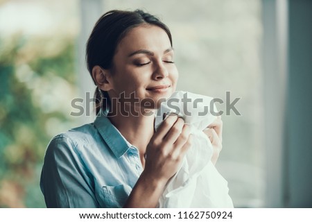 Young Pretty Smiling Woman Smeling Clean Clothes. Portrait of Happy Beautiful Girl enjoying Smell of Fresh Clothing just after Laundry. Young Attractive Woman doing Housework. House laundry
