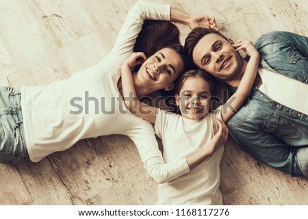 Happy Family Lying of Floor Together at Home. Beautiful Woman Handsome Man and Adorable Little Girl Lying on Parquet Floor and Hugging. Parents and Child Together. Family and Parenthood Concept