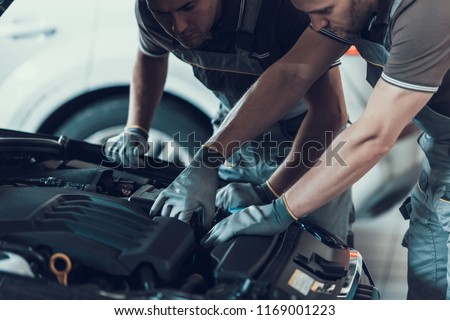 Close-up of Two Mecanics while Fixing Car. Strong Muscular Workers in Uniform and Gloves Repairing Automobile Engine with Opened Hood Posing with Serious Expression. Repair Service Concept