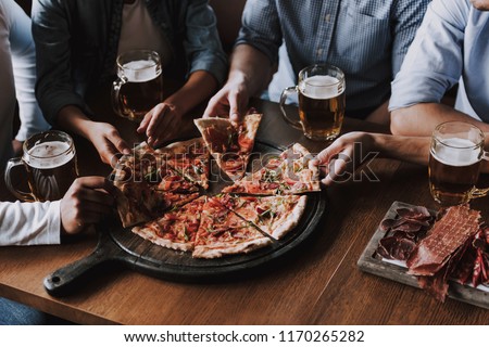 Close up of People Hands Taking Slices of Pizza. Smiling Friends Eating Pizza and Drinking Beer at Restaurant or Pizzeria. Friends Partying and Eating Pizza. Drinking Beer.